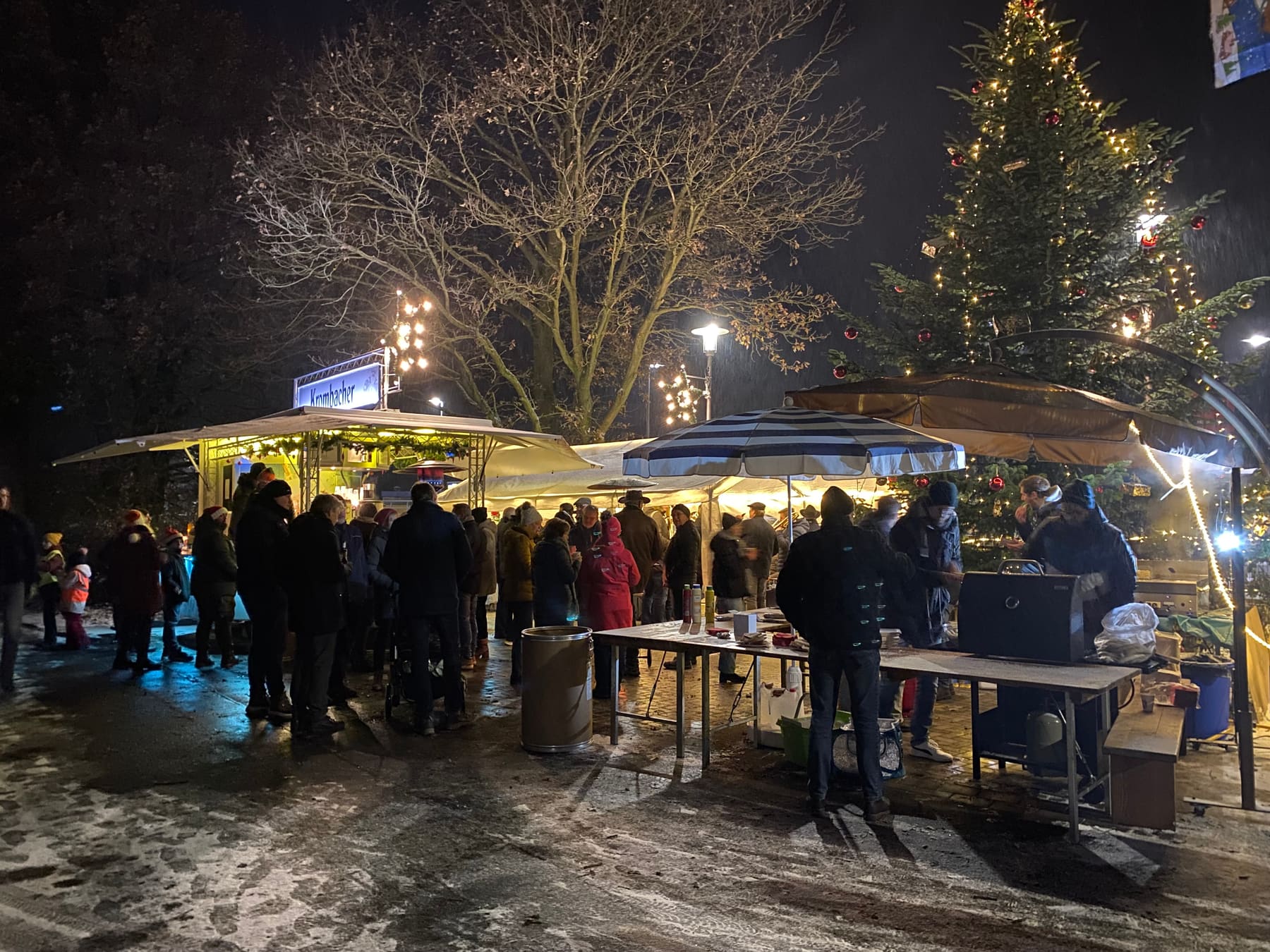 Abendlicher Adventsmarkt mit beleuchtetem Weihnachtsbaum und Ständen